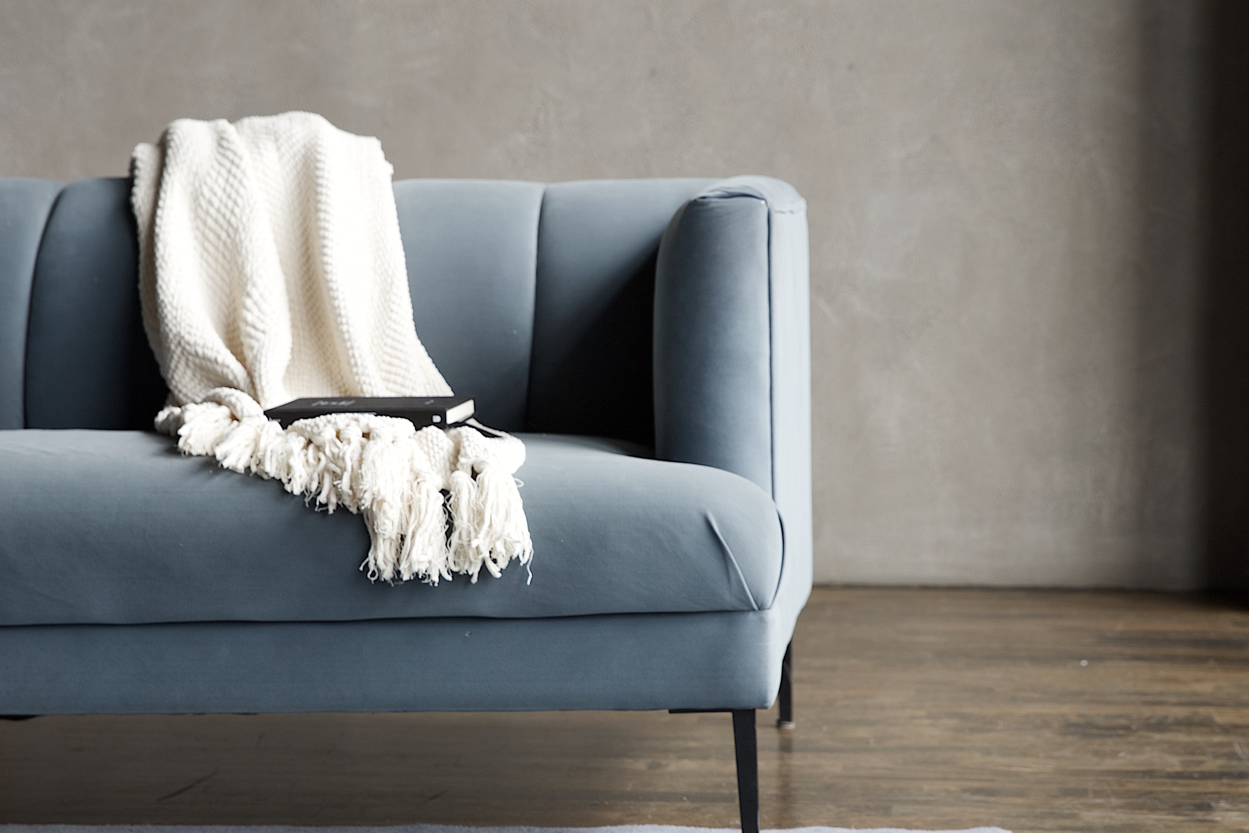 Gray sofa with a white blanket on a gray, modern style rug in a minimalistic, Toronto room.