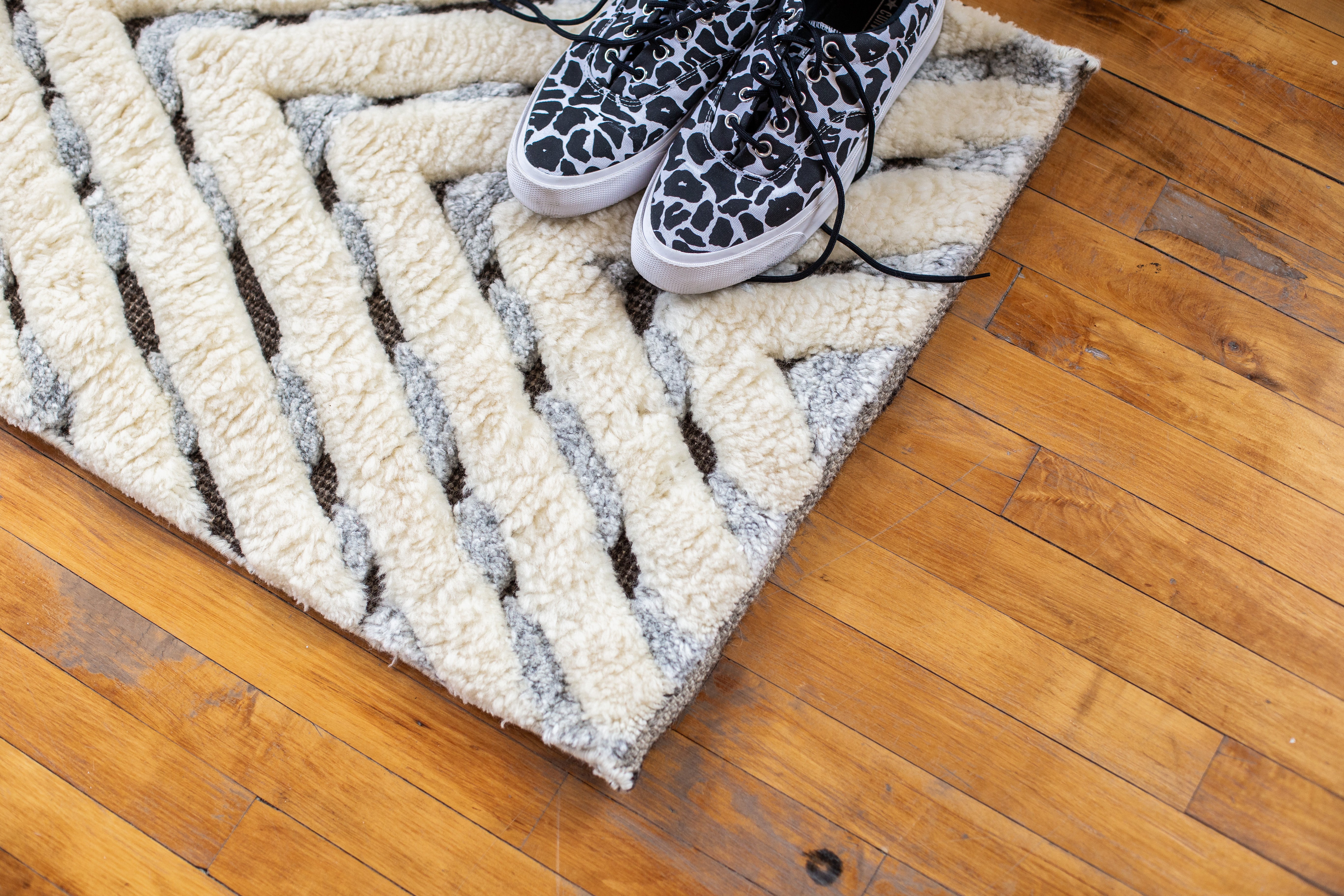 Textured, wool area rug with striped design on hardwood floor. Leopard print shoes placed on top of rug. Rug created by Studio321B, Toronto.