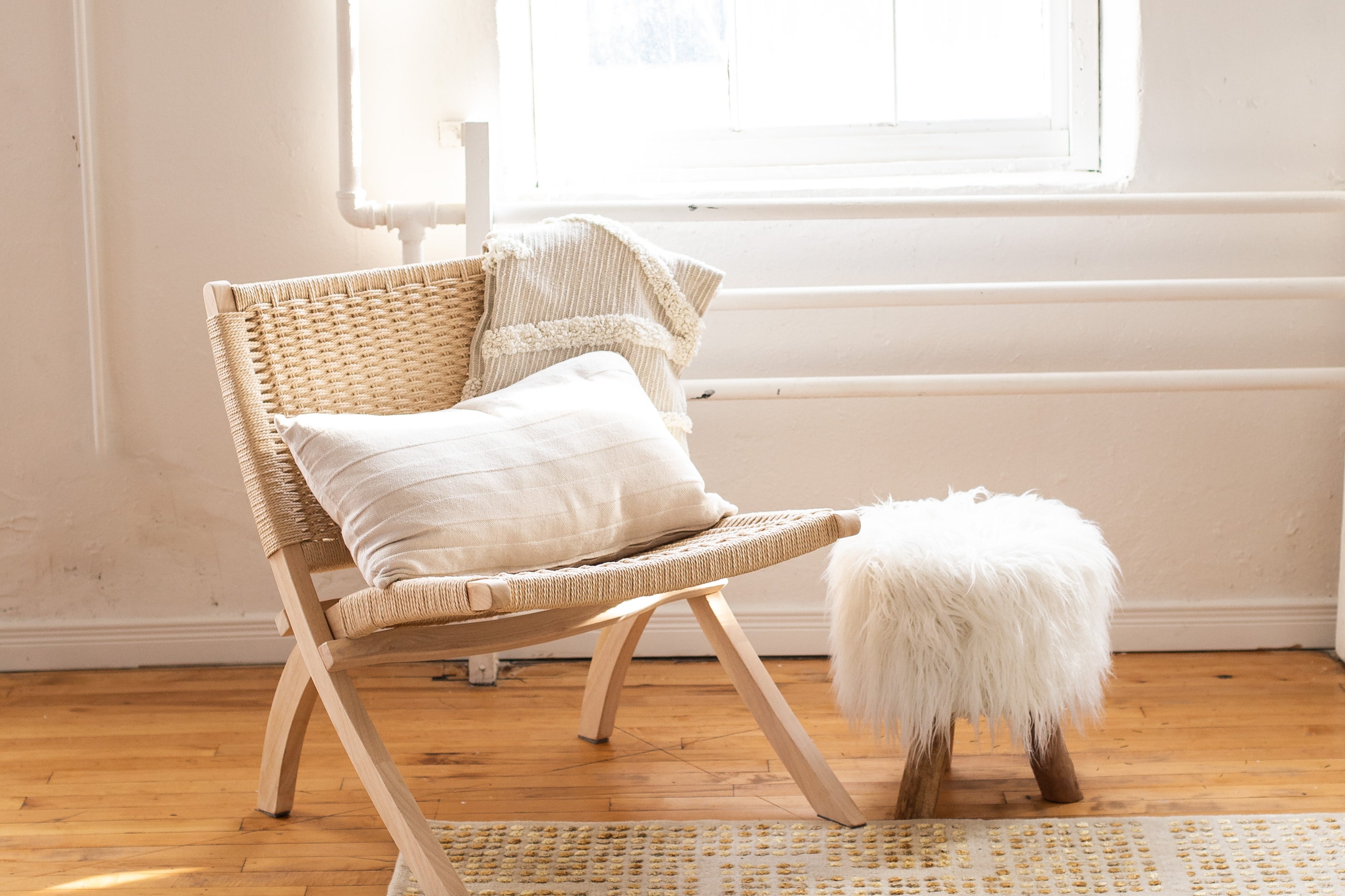 Wicker chair with a white pillow and small white ottoman on a white and tan woven rug in a bright room. Rugs in Toronto, Ontario.