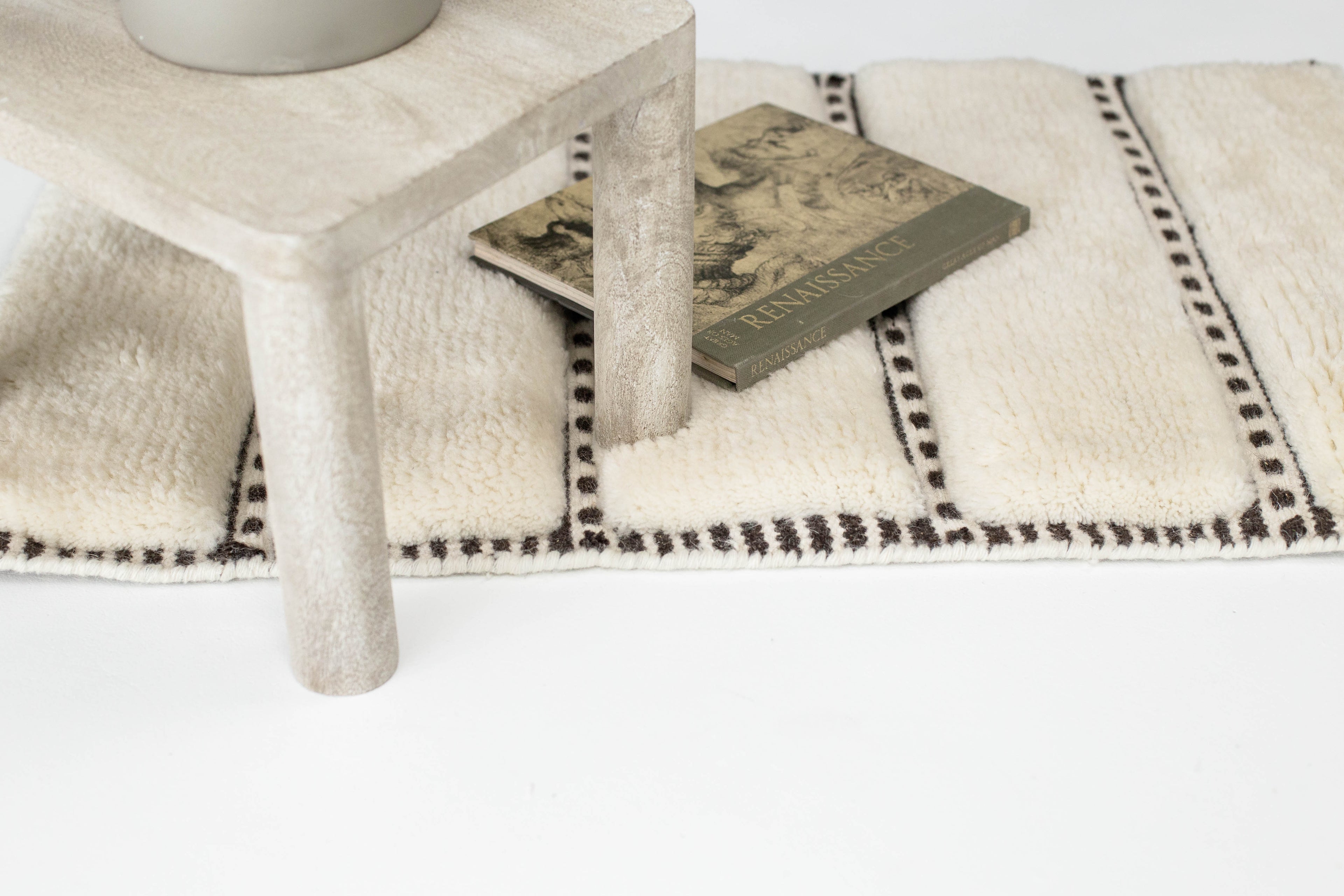 Contemporary wool rug in Toronto, Ontario showroom featuring black grid design and neutral tones. Styled under a stone side table in a modern interior. Created by Studio 321B Toronto.