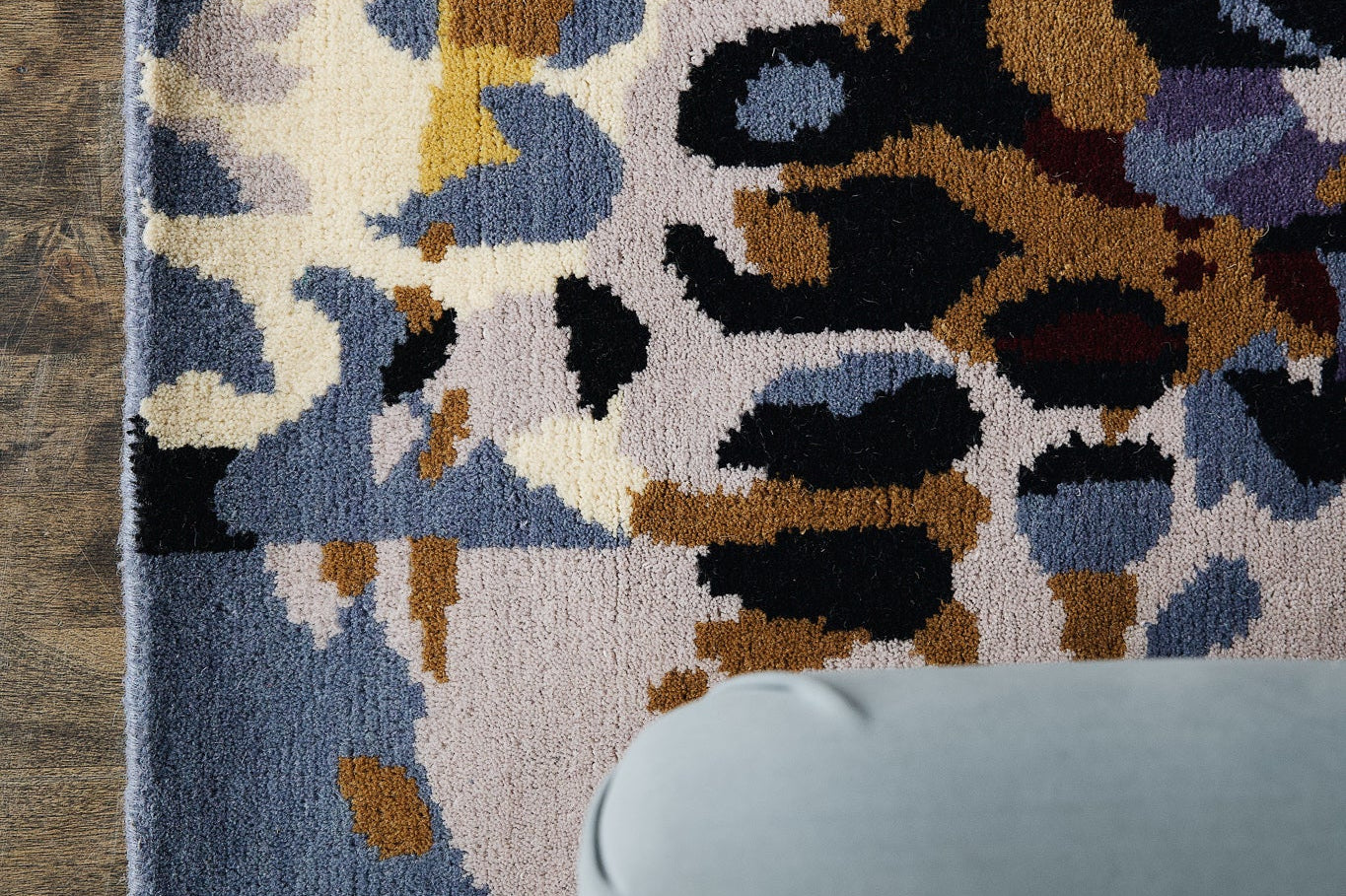 Multicoloured rug being used as wall decor behind a blue couch.